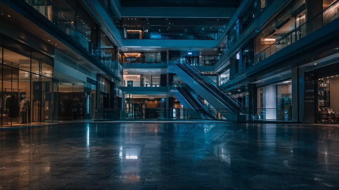 A shopping mall atrium after closing, shop lights still on across four levels